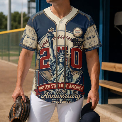 A male model wearing the custom cream and navy Statue of Liberty USA 250th anniversary baseball jersey standing inside a baseball field dugout.